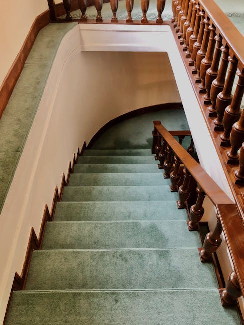 Close-up view of a beige carpet with a decorative floral pattern in dark brown, focusing on the corner of the rug where signs of mould are visible along the edges. The surrounding area features a clean, light-colored tiled or vinyl floor, with natural daylight illuminating the scene. The image highlights the importance of surface cleaning and routine maintenance in residential settings, as part of deep cleaning and sanitisation efforts, with the company Pimlico Carpet Cleaning potentially offering solutions for mould remediation on carpets in Pimlico flats.