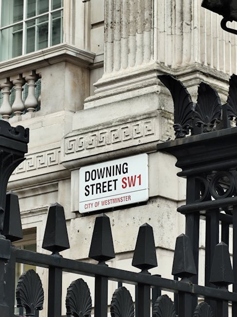 A street scene outside Westminster Station featuring the iconic London Underground sign suspended above a black-and-white sign indicating the station's name and facilities, including public subway and toilets. The background shows historic university or government building facades with detailed stonework, lampposts with spherical lamps, and a Union Jack flag flying nearby. The sky is clear with bright sunlight illuminating the area, and the street appears clean and well-maintained. This image showcases an outdoor urban setting associated with Westminster in London, emphasizing historic architecture and public transport signage, consistent with the theme of surface cleaning and maintenance by Pimlico Carpet Cleaning.